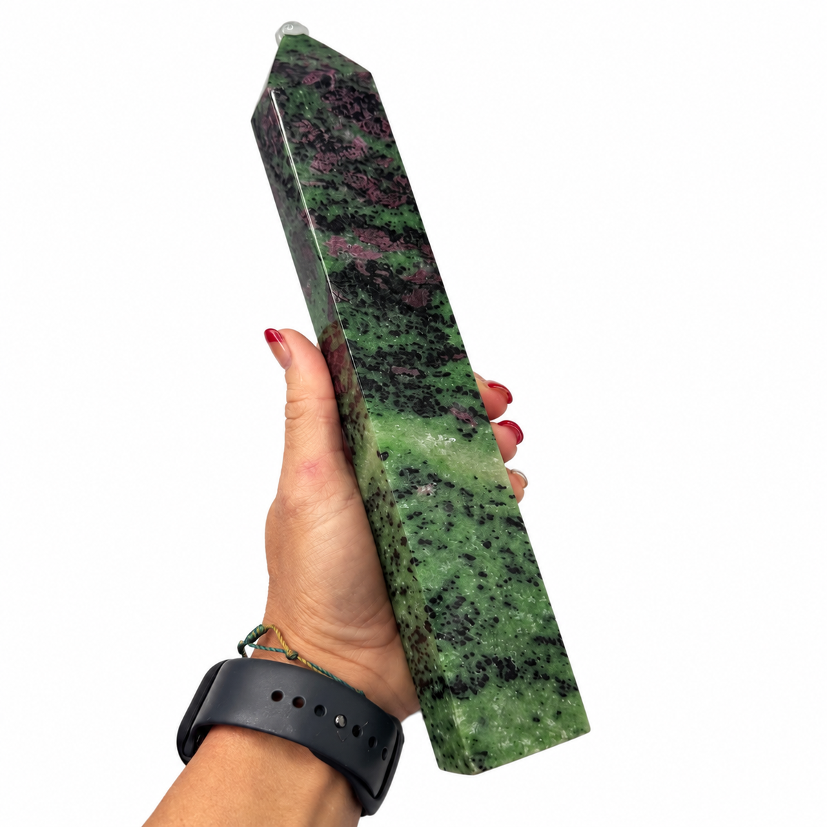 A hand holding a polished green and black natural stone obelisk against a plain white background.