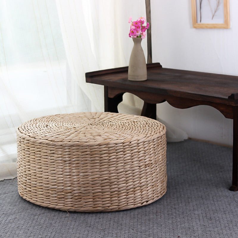 Woven ottoman in front of a wooden table with a vase and flowers on a light background