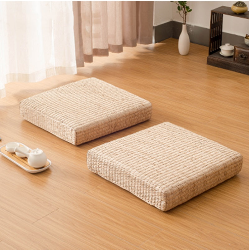 Two beige floor cushions on a wooden floor with a tea set and decorative items in the background.