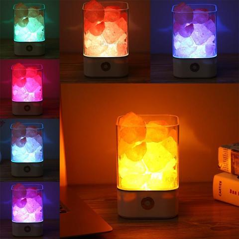 Colorful rock salt lamps emitting different hues on a wooden surface.