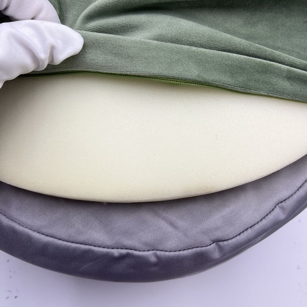 Close-up of a foam cushion with a green cover and gray border, held by a gloved hand.