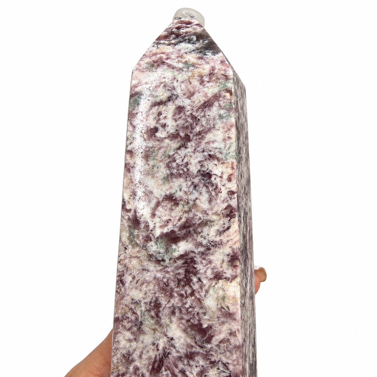 A hand holds a large, polished natural quartz crystal obelisk with a marbled pattern of purple, white, and green.