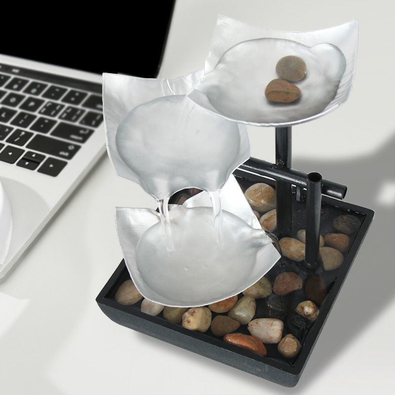 Feng Shui three-tiered water fountain with pebbles on a desk next to a laptop.