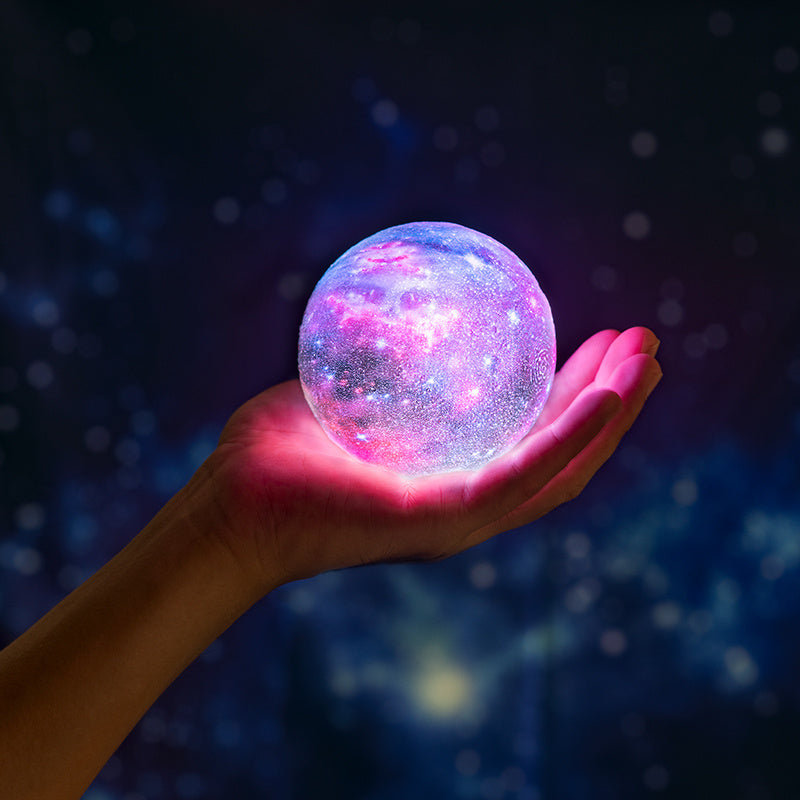 Hand holding a glowing crystal ball with a starry design against a dark background