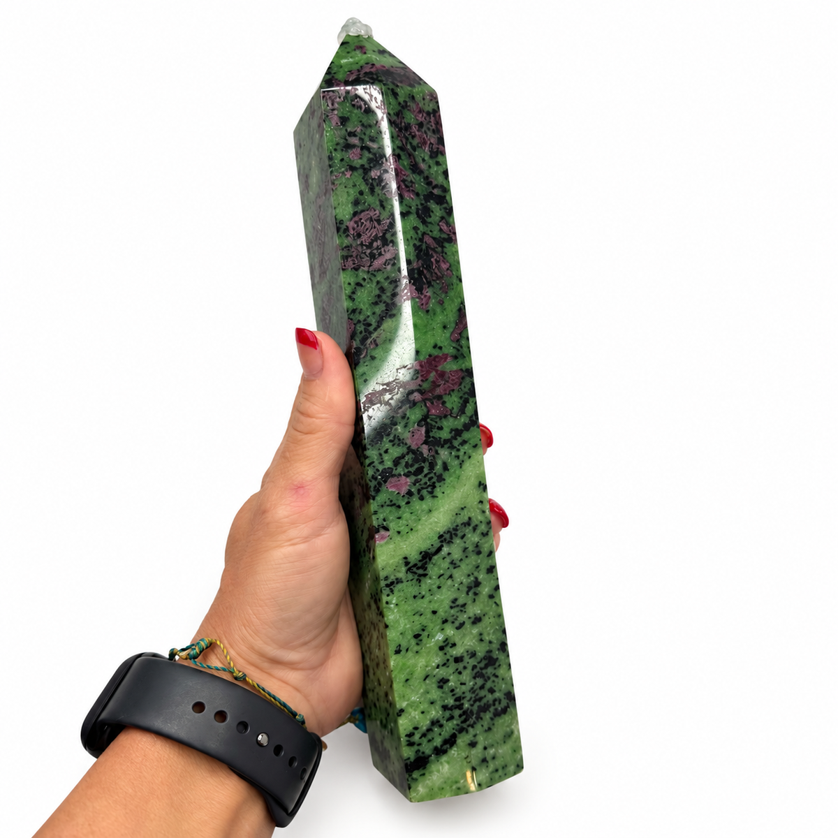 A hand holding a polished green crystal tower with black and purple mottled patterns, shown against a plain white background.