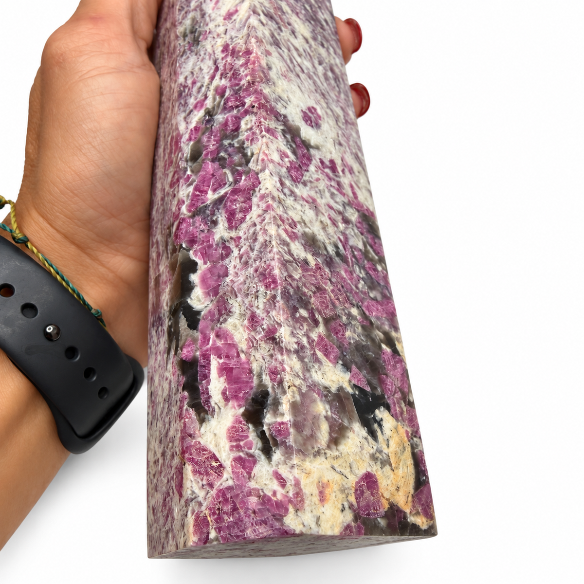 A hand holding a large polished cylindrical stone slab with a mottled pattern of magenta-purple, cream, gray, and black mineral inclusions, shown against a plain white background.