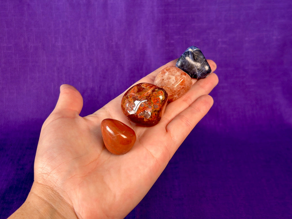 A hand holding four gemstones against a purple background.