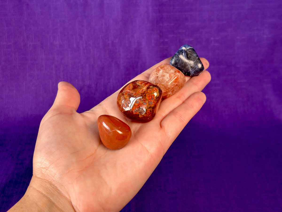 A hand holding four gemstones against a purple background.