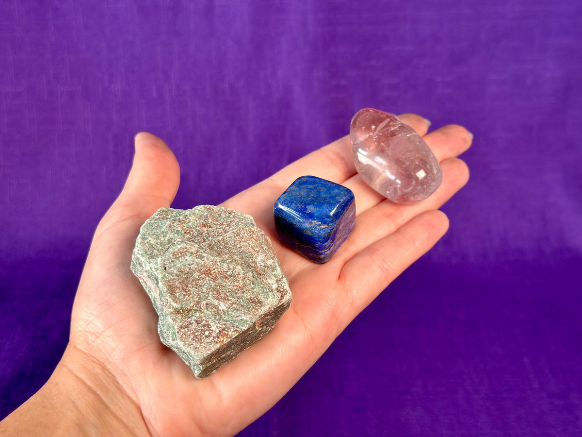 A hand holding three gemstones in front of a purple background.