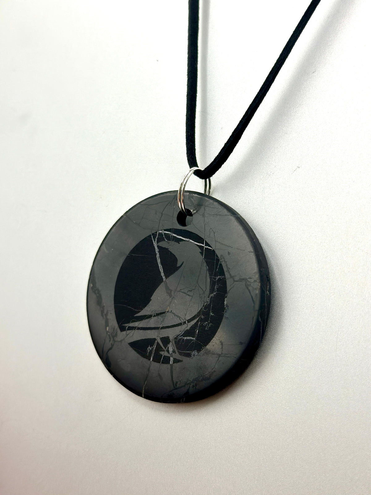 A black oval pendant necklace featuring a carved bird design on a black cord, displayed against a plain white background.