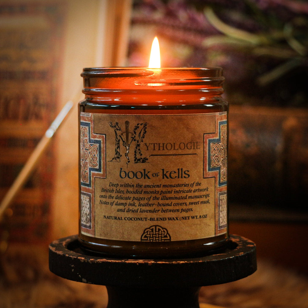 Candle in a jar labeled 'Mythologie book of kells' with a warm glow against a blurred background.