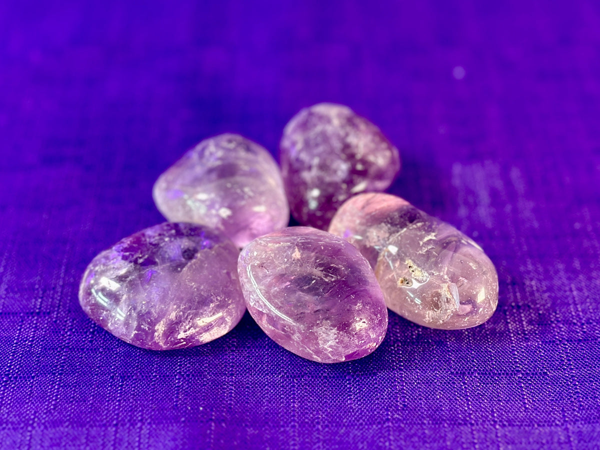 Five polished purple amethyst tumbled stones clustered together on a textured purple fabric background.
