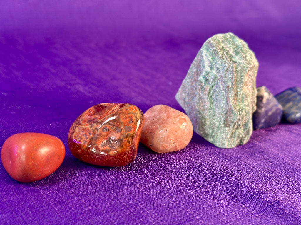 A set of polished and rough natural stones arranged on a textured purple fabric background.