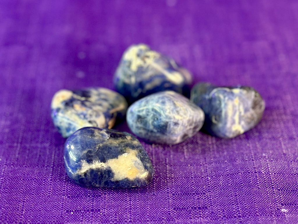 Five polished blue and cream tumbled stones arranged on a textured purple fabric background.
