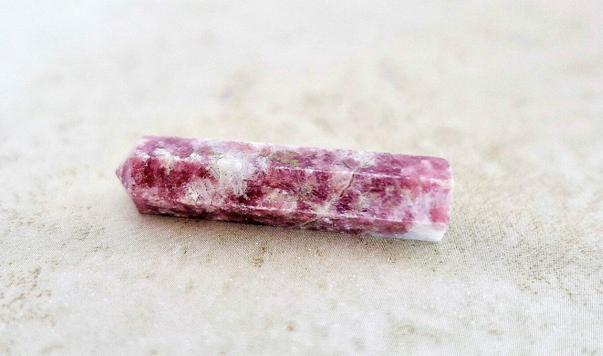 A Lepidolite Obelisk Crystal Gem wand lying horizontally