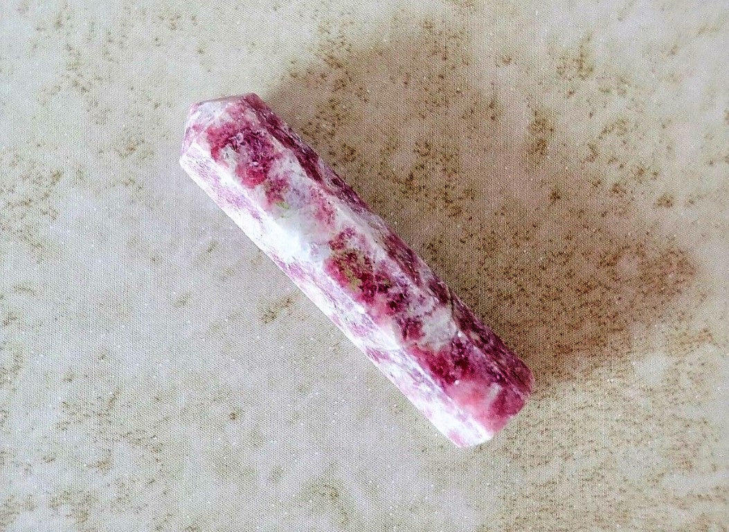 A Lepidolite Obelisk Crystal Gem wand on a fabric background 