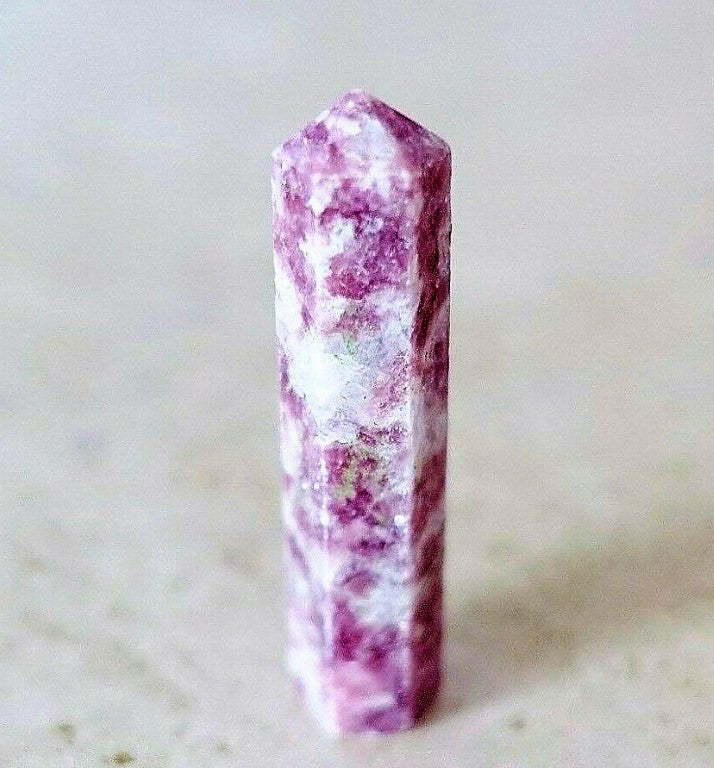 A Lepidolite Obelisk Crystal Gem wand standing on a light background