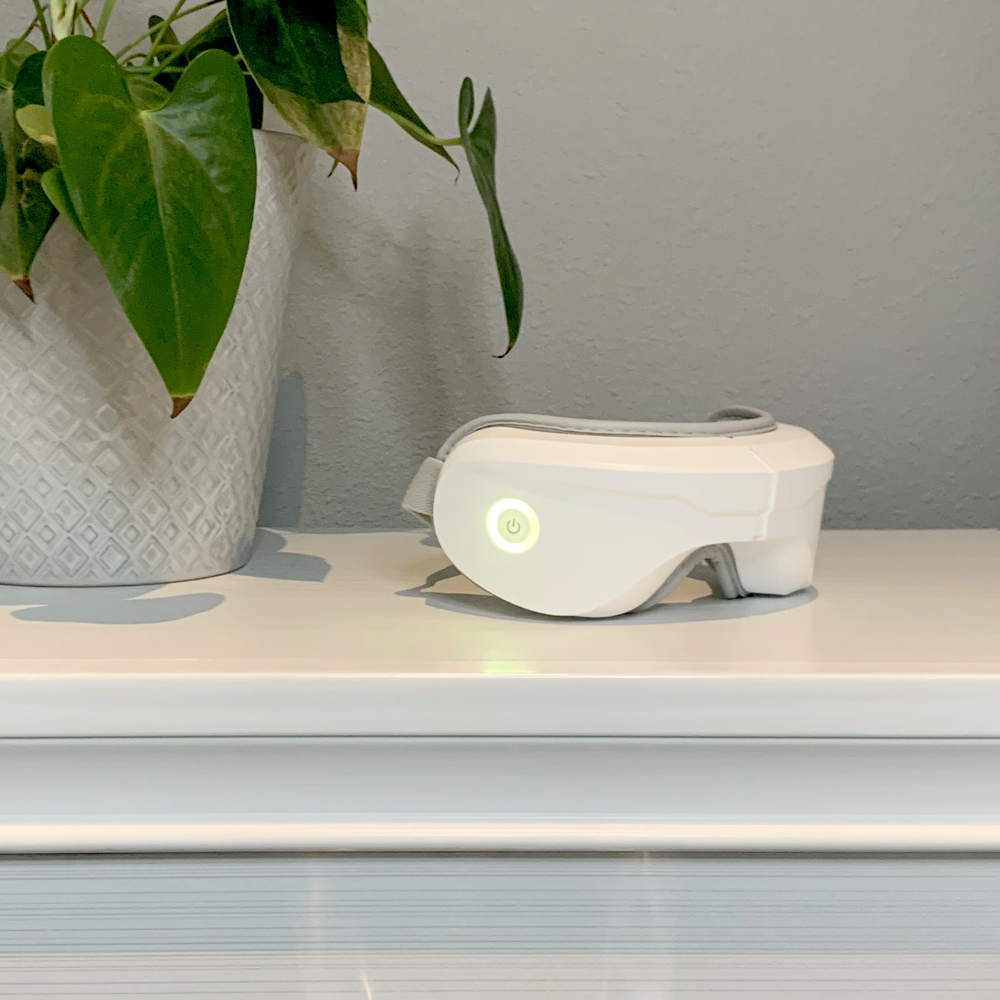 White electronic device with green light on a shelf next to a potted plant