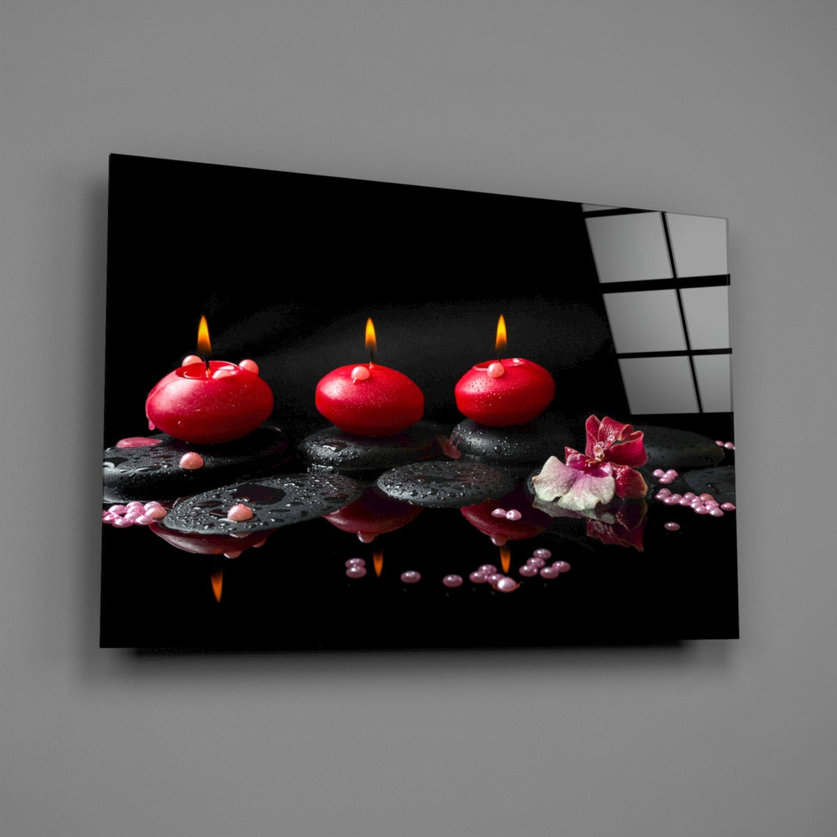 Black glass wall art showing three lit red candles on a white wall with dim lighting.