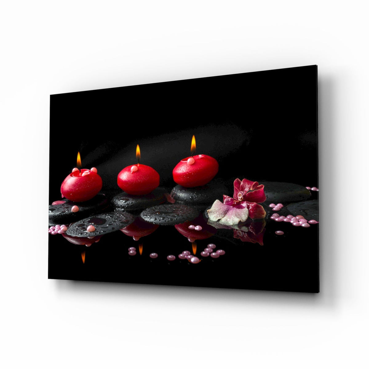 Black glass wall art showing three lit red candles on a white wall.