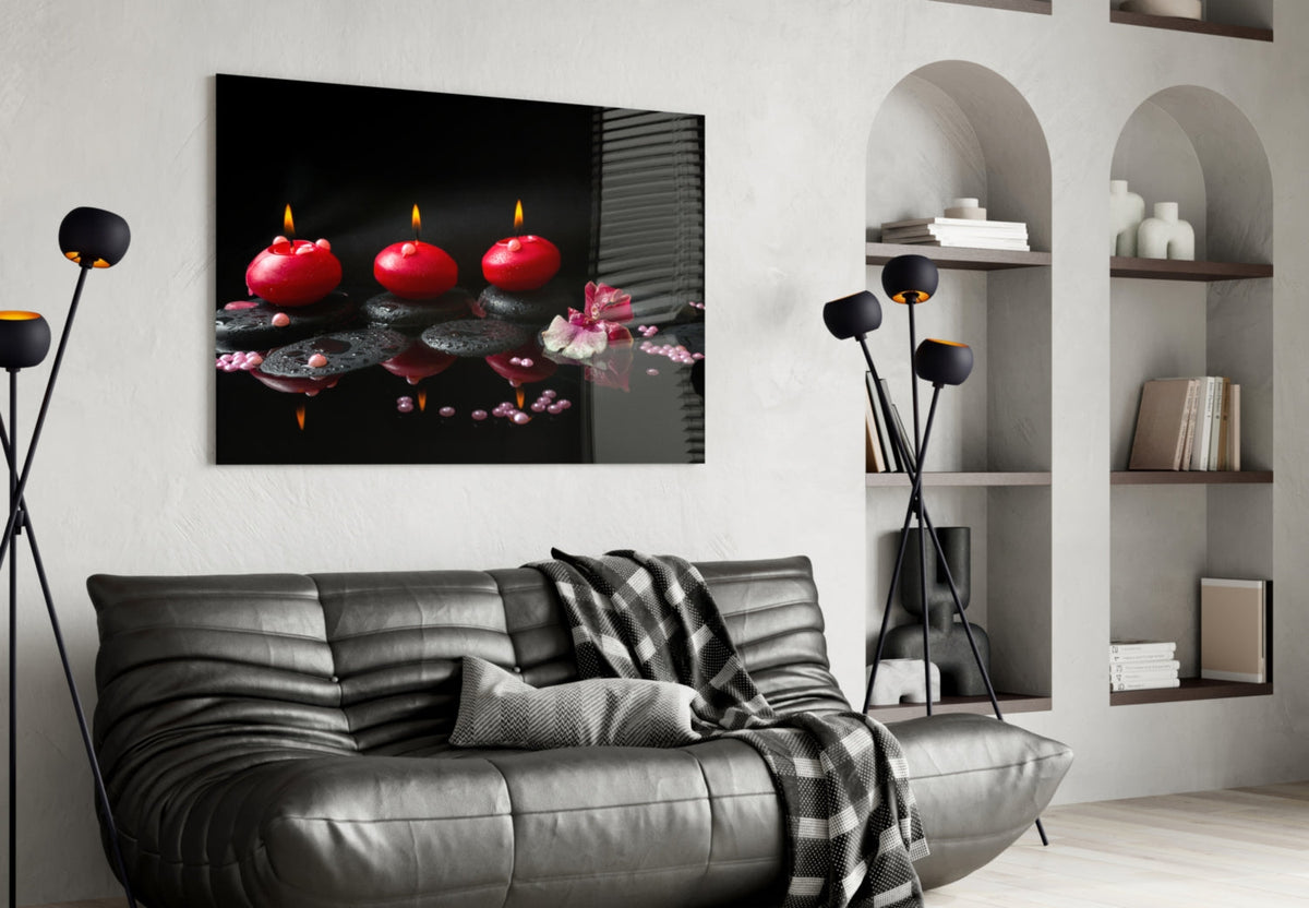 Black glass wall art showing three lit red candles on a white wall  over  black sofa.