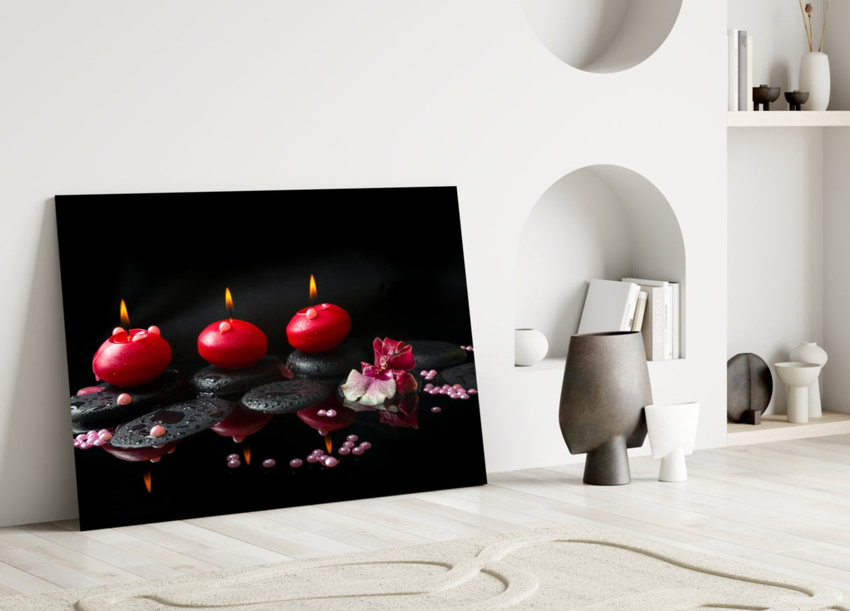 Black glass wall art showing three lit red candles sitting on a beige colored floor and leaning against a white wall.