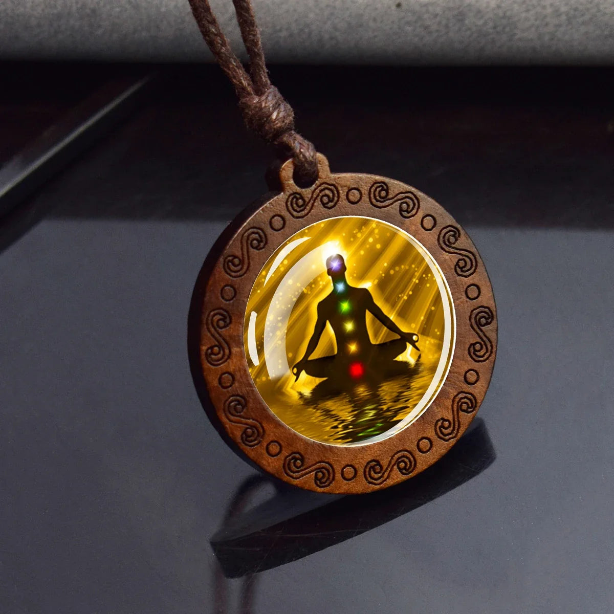 Wooden pendant with a meditating figure and chakra colors on a reflective surface
