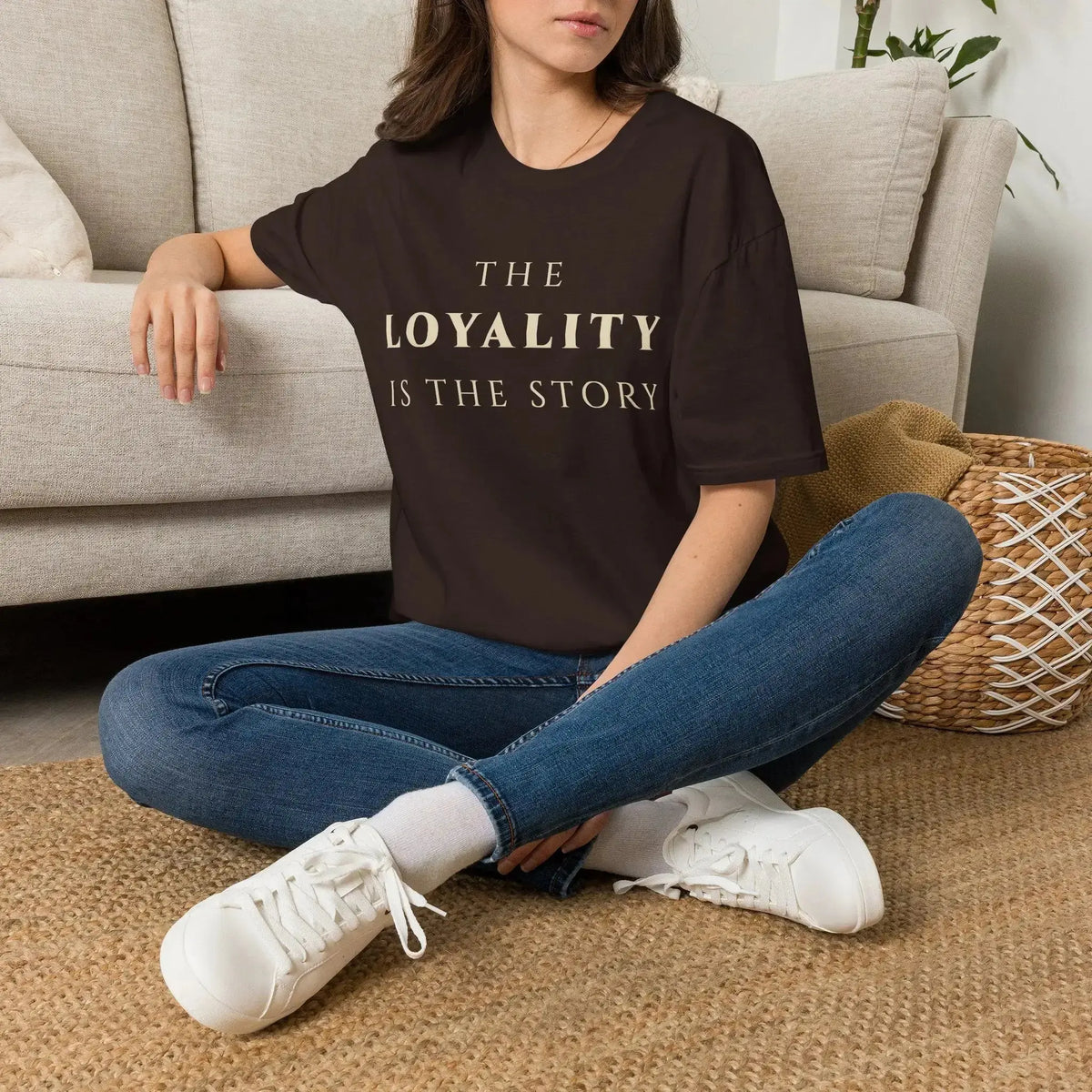 Person wearing a brown t-shirt with graphic design sitting on the floor in a living room.