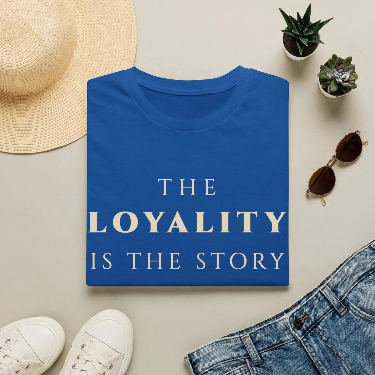 Blue t-shirt with 'The Spirituality is the Story' text, surrounded by casual items on a light surface.
