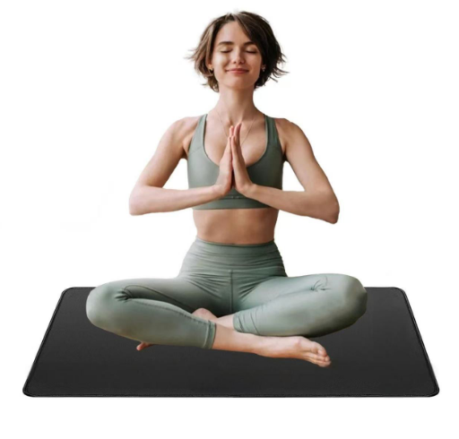 A woman in sage green activewear sits cross-legged on a black yoga mat against a plain white background, holding her hands together in a prayer pose.