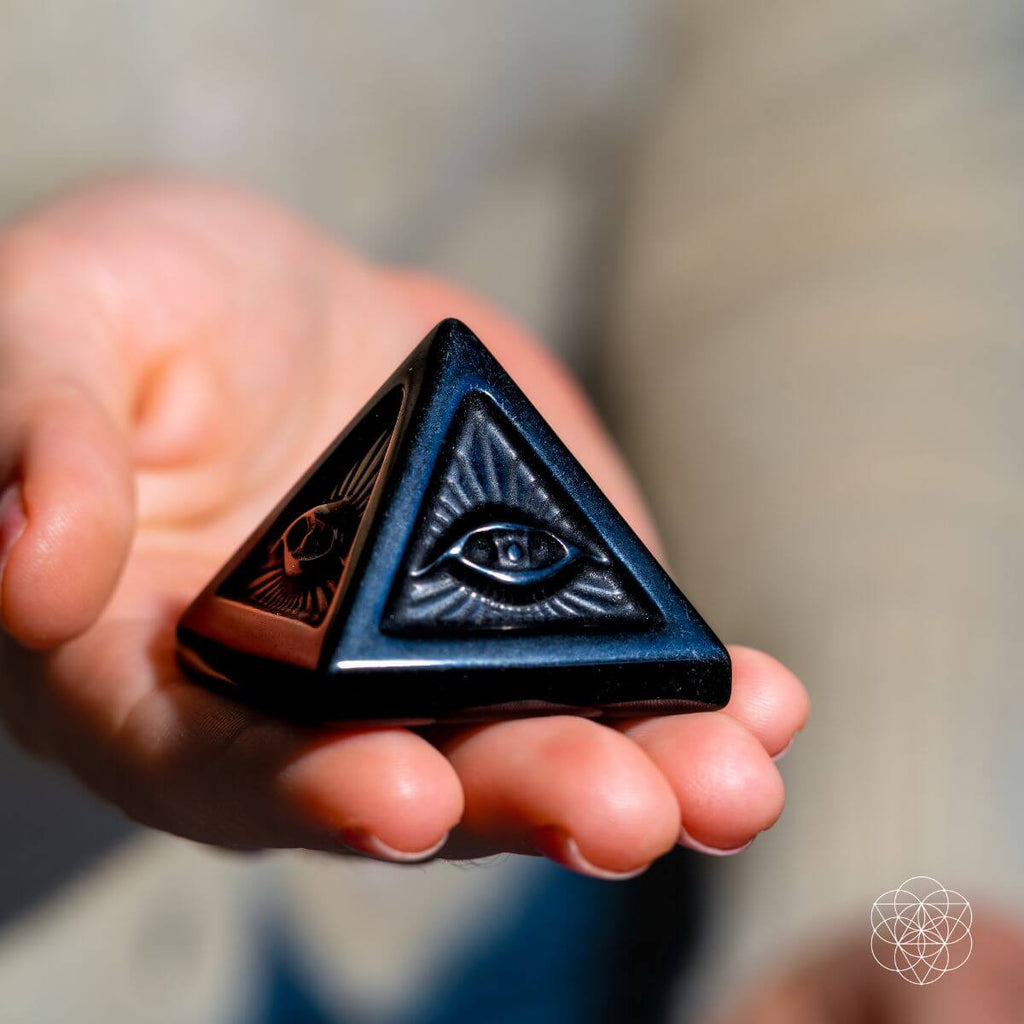 Hand holding a triangular object with eye design against a blurred background