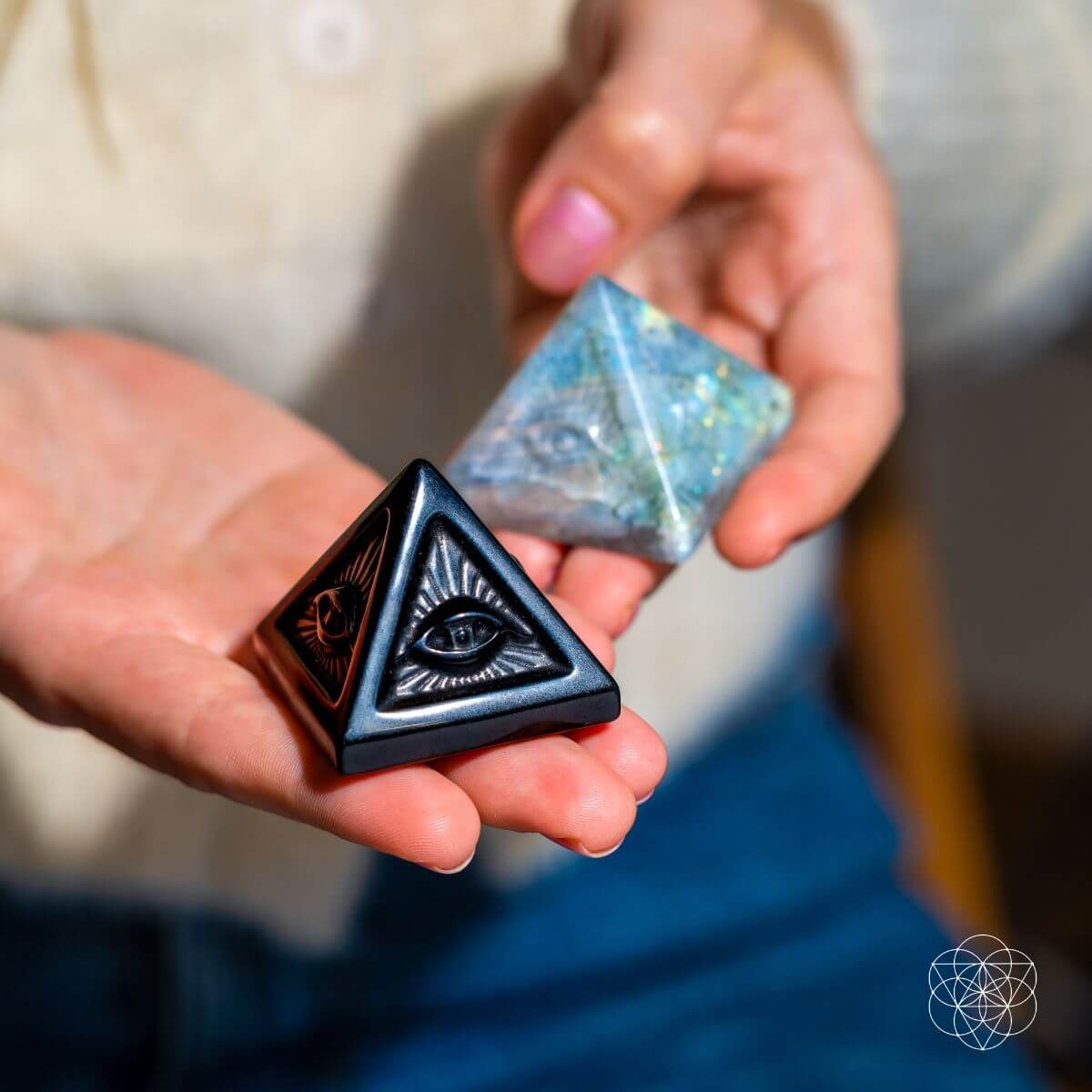 Person holding a black pyramid-shaped object with eye design and a blue crystal.