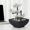 Decorative indoor water fountain with three tiered bowls on a white surface next to a laptop.