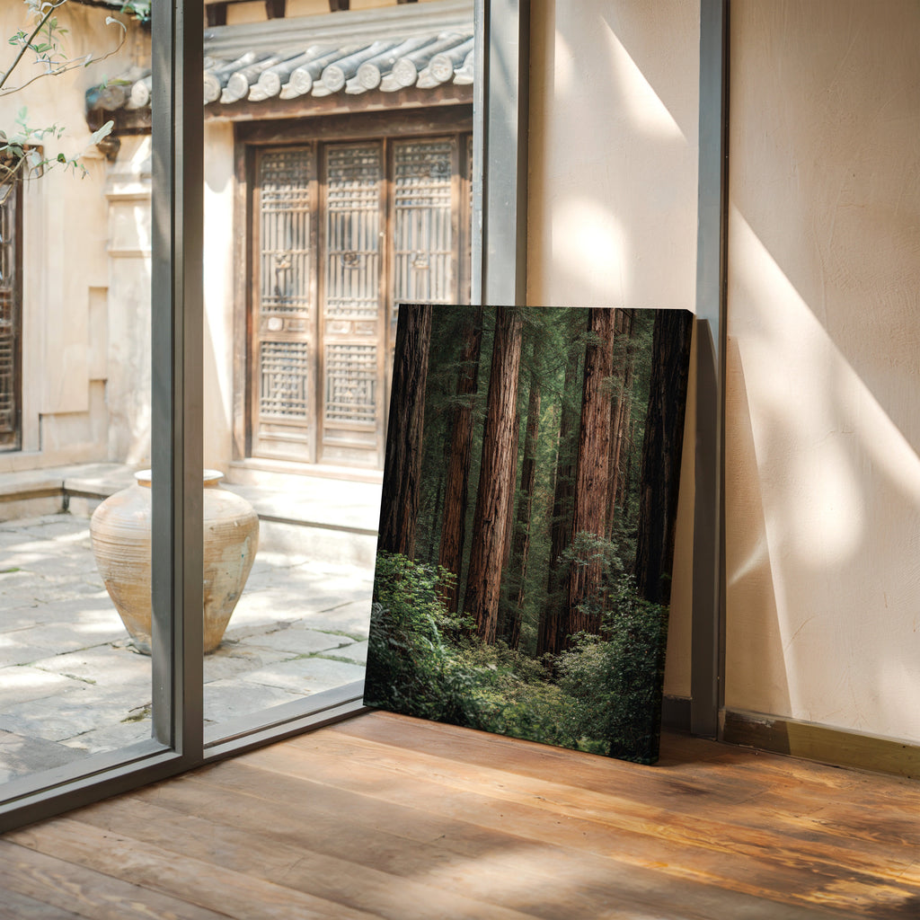 Framed photograph of a forest displayed in a room with wooden flooring and glass doors.