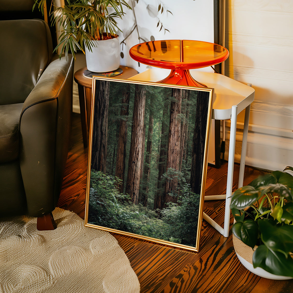 Framed nature print on a wooden floor with a chair and plants in the background