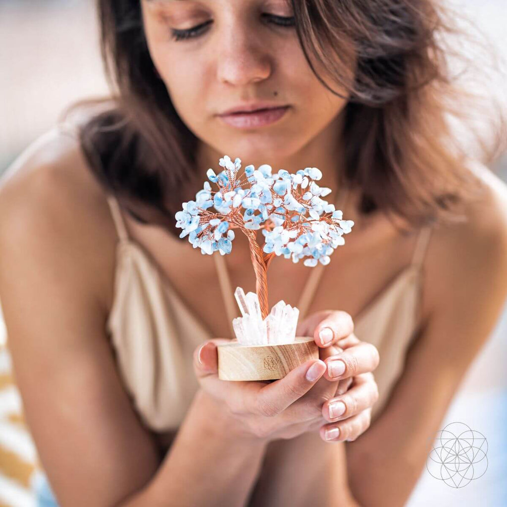Woman holding a small decorative tree with blue flowers and crystals.