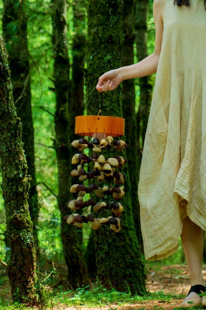 Picture of a woman holding a seed pod wind chime with her right hand in a wooded area.