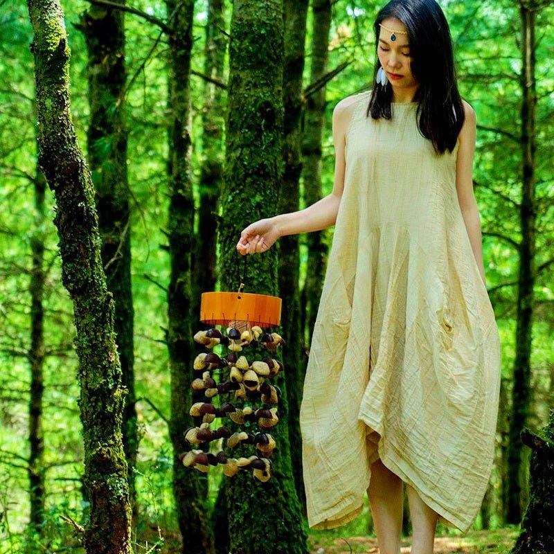 Picture of a woman holding a seed pod wind chime in a wooded area.