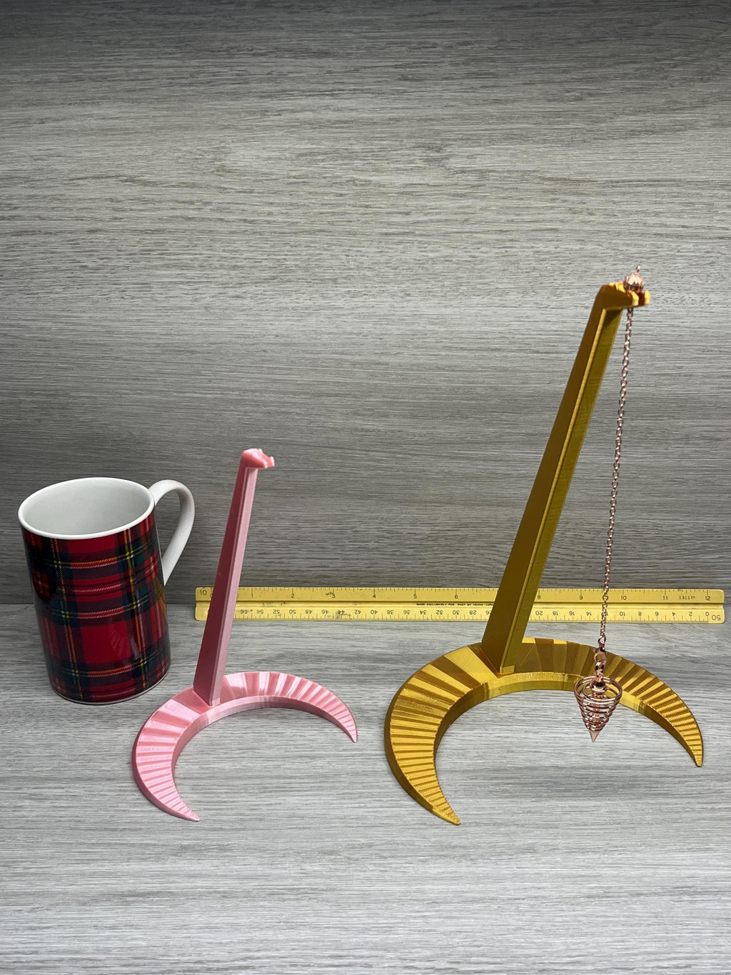 A Large and small Pendulum Moon Stand next to a ruler and a coffee cup.