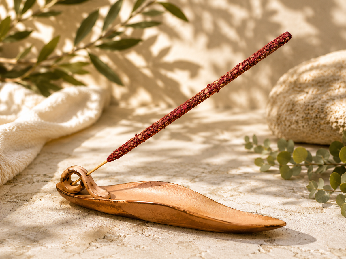 Incense burner shaped like a leaf holding a reddish incense stick