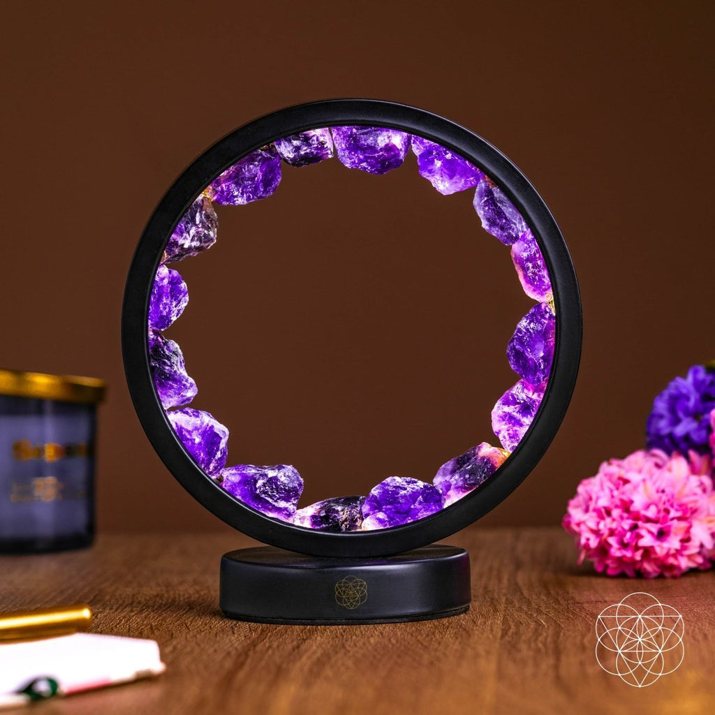 Picture of an Amethyst halo lamp on a wooden surface next to a couple of pink and purple crystals.