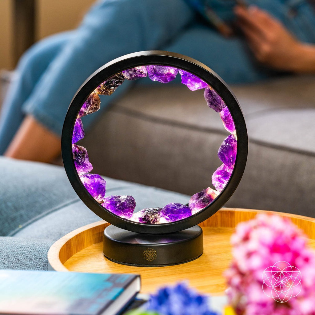 Picture of an Amethyst halo lamp sitting on a wooden tray with colorful flowers in front of a person sitting on a couch.