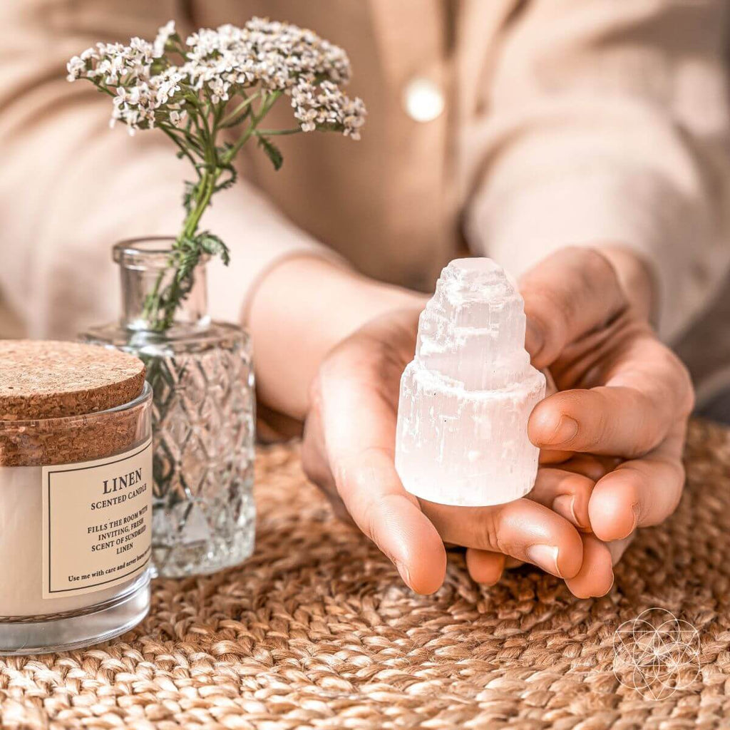 Person holding a small crystal sculpture with a candle and vase in the background