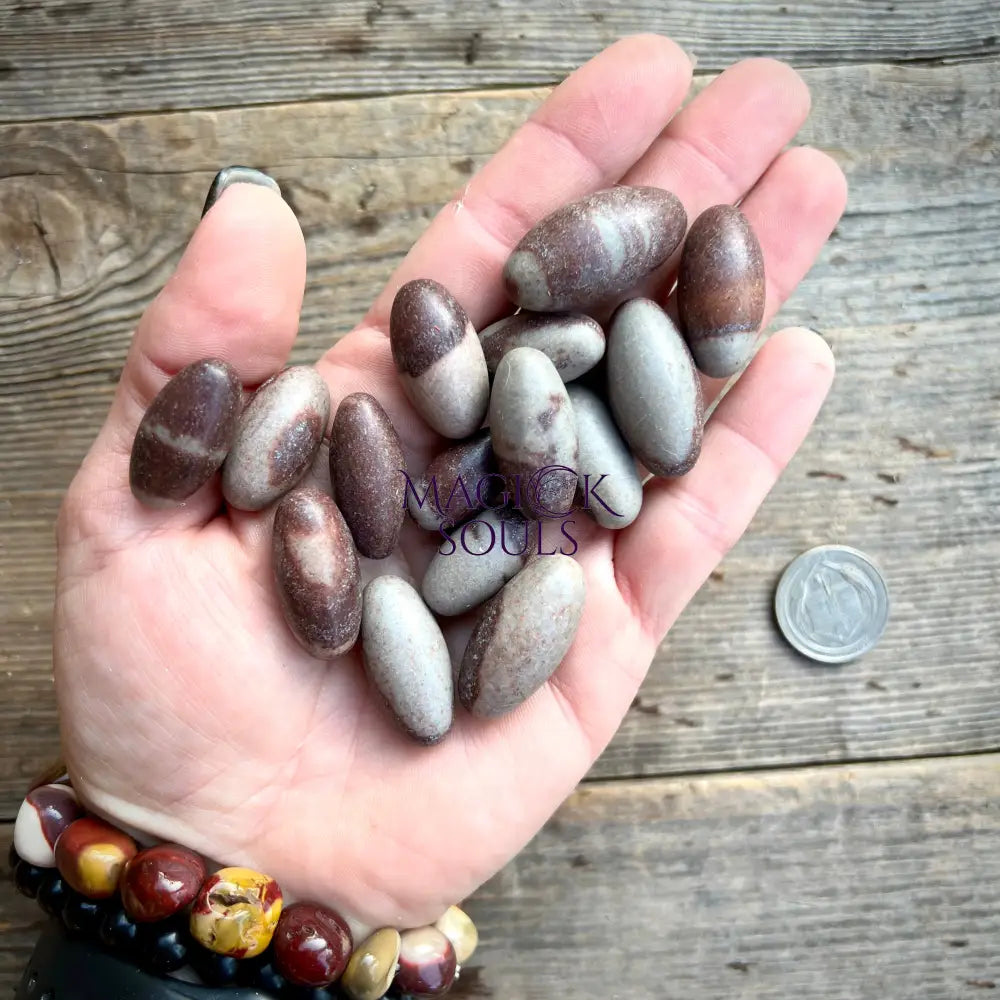 Hand holding a collection of smooth, polished stones on a wooden surface with 'Mack & Soul' branding.