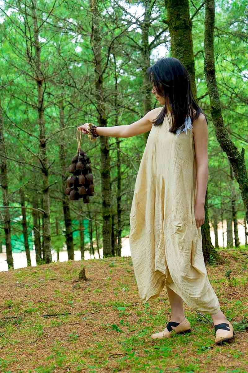 Woman in a beige dress holding a bundle of twigs in a forest setting